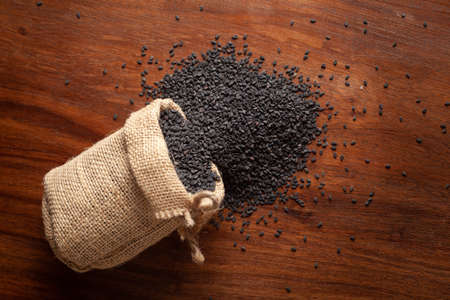 Close-up of  Organic Black Sesame seeds (Sesamum indicum) or Black Til with shell spilled out from a laying jute bag over a wooden brown background.の写真素材