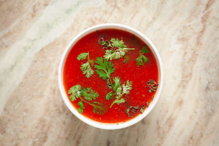 Close-up of Indian Homemade fresh tomato soup garnished with fresh coriander leaves and dry mint or...