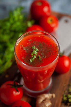 Close-up of Indian Homemade fresh and healthy tomato soup garnished with fresh coriander leaves and ingredients and herbs, served in drinking glass over the wooden top background.の写真素材