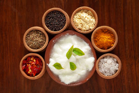 Close-up of Indian kadi or kadhi pakora with it basic ingredients. Garnished with green curry-patta leaves and red chili flacks. Over wooden top background.の写真素材