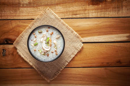 Close-up of Creamy Sabudana Kheer Garnished with dry fruits. Indian delicious dessert. Served in a black bowl. Top View on wooden background.の写真素材
