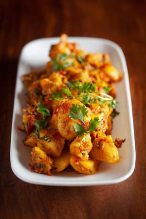 Macro Close-up of Indian vegetarian dish of spicy Potato and Tomato curry garnished with green coriander fresh leaves.の写真素材