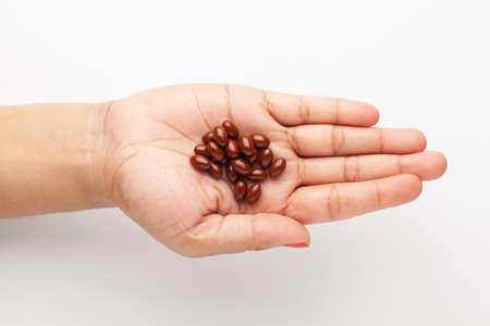 Macro Close up of medicinal or herbal dark red-brown pill on female hand palm. Top view, white...