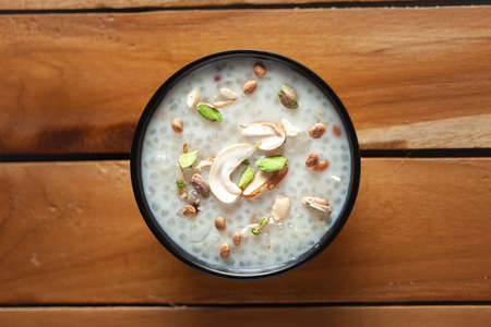 Close-up of Creamy Sabudana Kheer Garnished with dry fruits. Indian delicious dessert. Served in a black bowl. Top View on wooden background.の写真素材