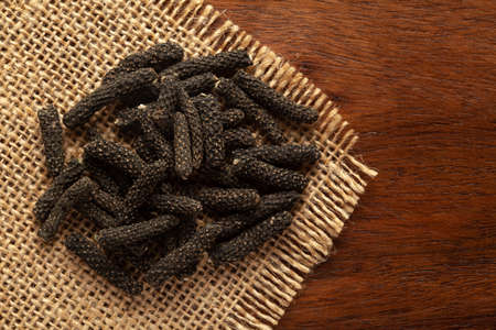 Macro close-up of Organic Indian long pepper  (Piper retrofractum ) on the wooden top background and jute mat. Pile of Indian Aromatic Spice. Top viewの写真素材