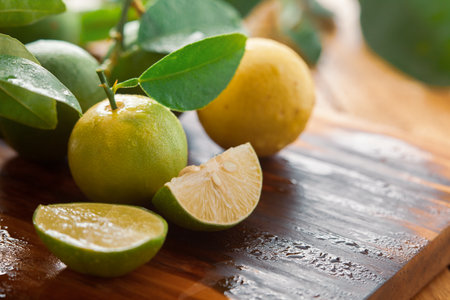 Close-up of fresh green and yellow  organic lemon (Citrus limon) and slices and pieces of lemon on a wooden cutting board with green leaf.の写真素材