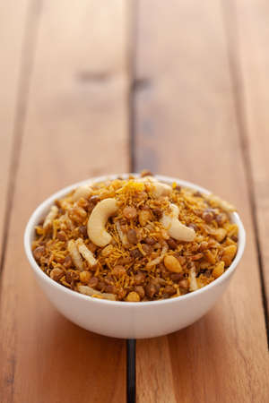 Close-Up of Dal Biji or Dal moth, made with roasted Masoor Dal (black lentils) and small besan sev, garnished with fried cashew nuts . Indian spicy snacks (Namkeen), in white ceramic bowl over wooden  backgroundの写真素材