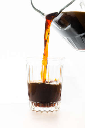 Black coffee poured from a jar into a cup on white background.