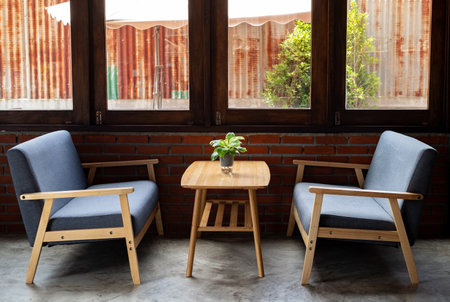 wooden sofa with soft cushions in gray, wooden ornaments sits on a wooden table by the window in a coffee shopの写真素材