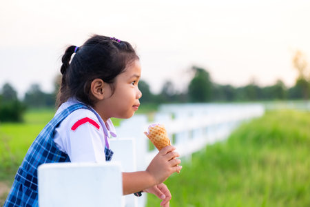 Cute Asian girl in school uniform eating ice cream while on vacation with family, and blured of green field rice  nature background, Happy family conceptの写真素材