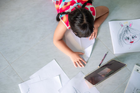 Asian girl, 5-6 years old, practicing origami using video clips or studying online via tablet at home, distance learning, education at home, work form homeの写真素材