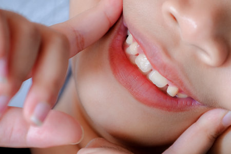 Close up of a cute Asian girl pointing her finger at the corner of her mouth and tilting her head to the right and smiling happily showing her front teeth. Happy life conceptの写真素材