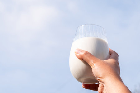 Mother hand holding a glasses of fresh organic white milk with green blue sky nature background and soft sunlight in the morning, healthy lifestyle daily concept, copy spaceの写真素材