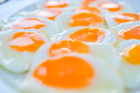 Close up of multiple sunny-side-up eggs with vibrant orange yolks and glossy whites, freshly cooked...
