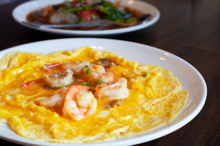 Delicious shrimp omelette served on a white plate. Freshly cooked eggs with juicy shrimp, perfect for breakfast or brunch. Tasty Asian-style seafood dish on wooden tableの写真素材