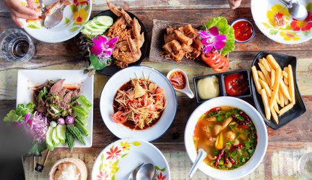 Top view of a colorful Thai meal with traditional dishes, fresh vegetables, fried chicken, papaya...
