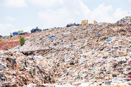 Large pile of plastic waste and garbage in an open landfill under cloudy sky, representing...