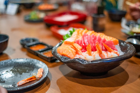 Fresh assorted sashimi platter with salmon, tuna, and shrimp served on crushed ice in a black bowl, showcasing vibrant colors and premium seafood for Japanese cuisine lovers.の写真素材
