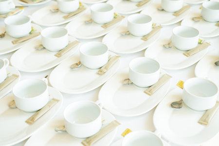 White ceramic coffee cups neatly arranged on white plates with spoons and sugar packets, ready for a...