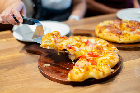 Close up of a person serving hot cheese pizza with a spatula in a restaurant. Freshly baked pizza topped with melted cheese and toppings, ideal for food, dining, and Italian cuisine concepts.の写真素材