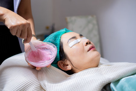 Close-up of a therapist's hand mixing a pink cosmetic facial mask in a glass bowl with a spatula for a client. Professional skincare preparation, treatment, and wellness concept at a luxury spa.の写真素材
