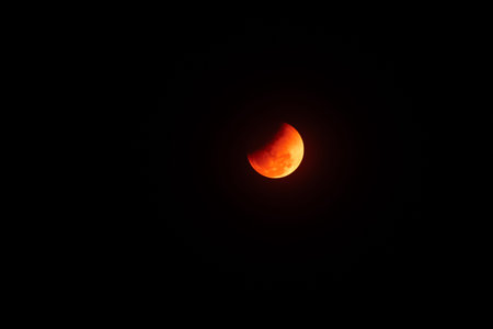Total lunar eclipse or blood moon glowing in the dark night sky. Mysterious orange full moon during...