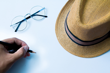 Top view of glasses , hat and Hand is writing on white  backgroundの写真素材