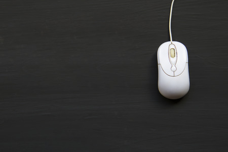 White computer mouse on the black wooden planks background.の写真素材