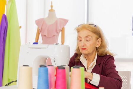 Professional female designers are sewing with small sewing machines on the table.