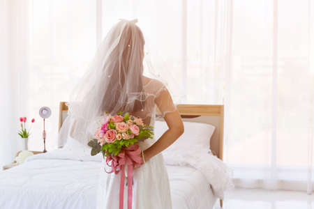 An Asian bride wore a white wedding dress, standing, holding a bouquet of beautiful flowers behind her.の写真素材