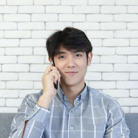 A young Asian man talking on his cell phone and smiling brightly.