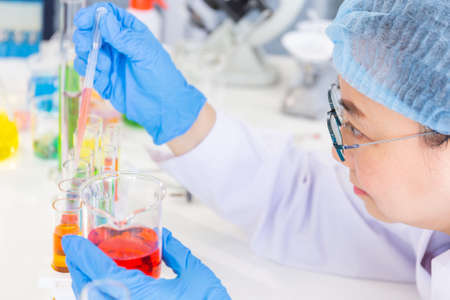 Discovering a cure for an Asian female scientist who is concentrated, holding a test tube and...