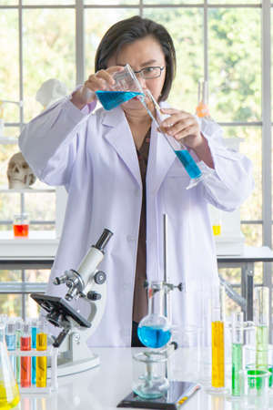 Discovering a cure for an Asian female scientist who is concentrated, holding a test tube and watching while working.の写真素材