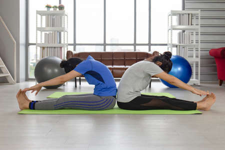 2 women doing yoga on a rubber mat inside her house.