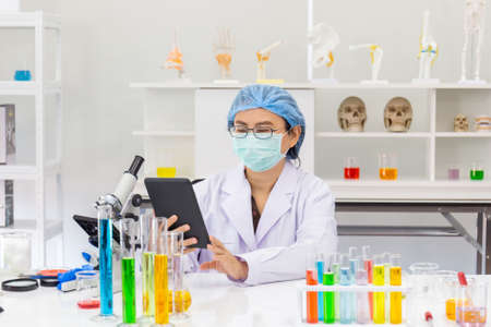 An Asian female scientist is researching a chemical formula in a lab in a hand held tablet.
