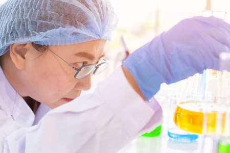 Discovering a cure for an Asian female scientist who is concentrated, holding a test tube and...