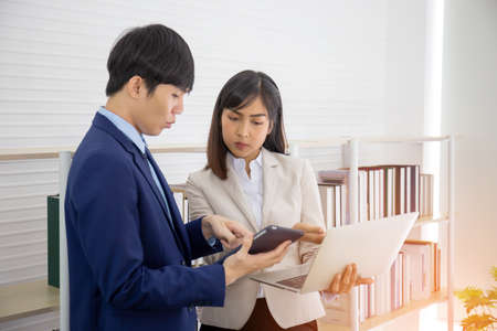 Two young Asian businessmen stand meeting in the office in the hand of the tablet.の写真素材