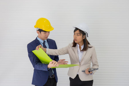 Two Asian male and female foreman wearing a helmet and standing and talking at the event siteの写真素材
