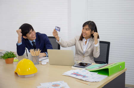 An Asian businesswoman looks happy in her hand, holding a credit card with a male staff member next to him.の写真素材