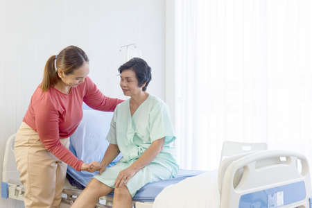 A young Asian woman who was ill in a hospital lay on a recovery bed. Her mother, who was taking care...