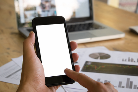 Woman with modern mobile phone in hands touching on a blank screen.Blurred office table on background.の写真素材