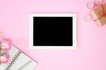 Tablet on centre with blank screen display Notebook and pen with pink rose flower on pink table.の写真素材