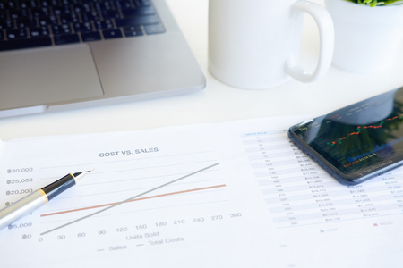 Cost financial concept, business equipment paper chart, pen with laptop computer and smartphone on office table.の写真素材