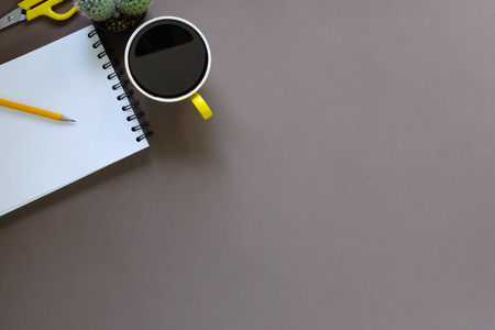 Office desk coffee cup and pencil with notepad paper on brown table background, Top view workspace.の写真素材