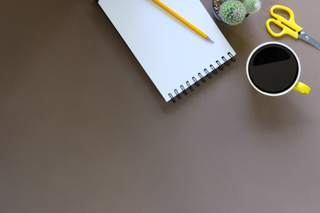 Office desk coffee cup and pencil with notepad paper on brown table background, Top view workspace.の写真素材