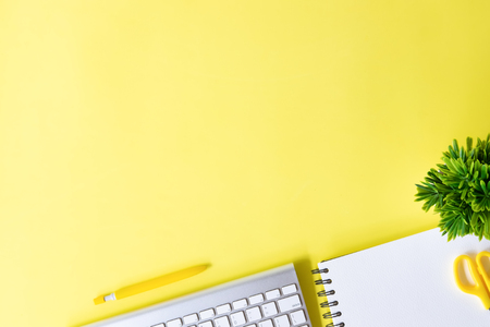 Above Office desk with computer keyboard, notebook paper, pen and plant decoration on yellow background top view mock up.の写真素材