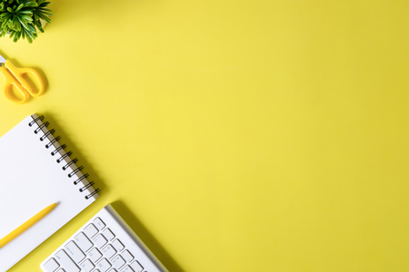 Above Office desk with computer keyboard, notebook paper, pen and plant decoration on yellow background top view mock up.の写真素材