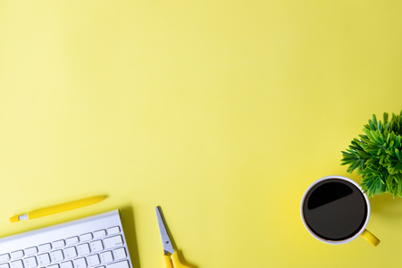 Office desk with computer keyboard, notebook paper, pen, coffee and plant decoration on yellow background top view mock up.の写真素材