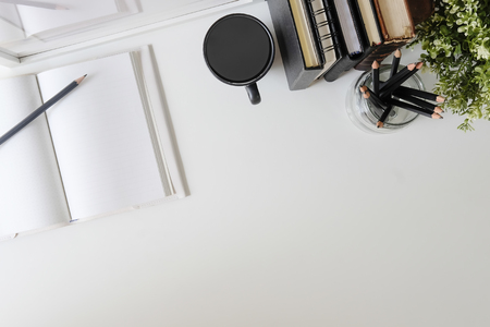 Flat lay, top view office table desk. Workspace with notebook, book, office supplies, pencil, green leaf, and coffee cup on white desk.の写真素材
