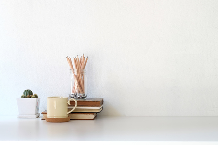 Workspace coffee mug, books, pencil and cactus on white desk.の写真素材